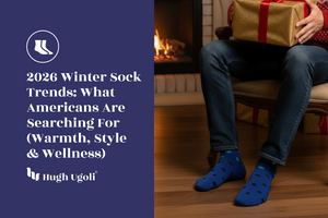 Man sitting by a fireplace holding a gift, wearing blue Hugh Ugoli socks, illustrating 2026 winter sock trends focused on warmth, style, and wellness in American households.