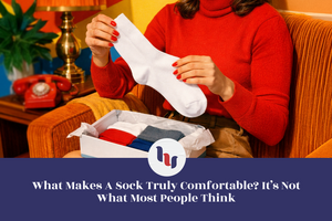 Person sitting in a vintage-style living room holding a plain white sock with both hands, with an open box of folded socks on their lap and warm retro decor in the background