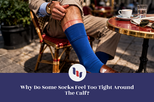 Person sitting at an outdoor cafe with a blue sock on their calf, wearing a beige jacket and brown shoes.