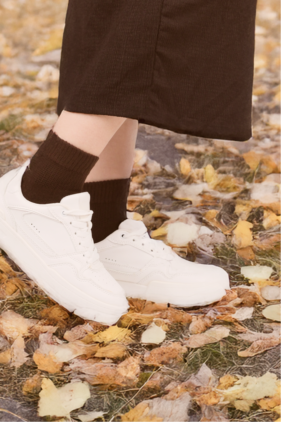 White sneakers with dark socks on a ground covered with fallen leaves