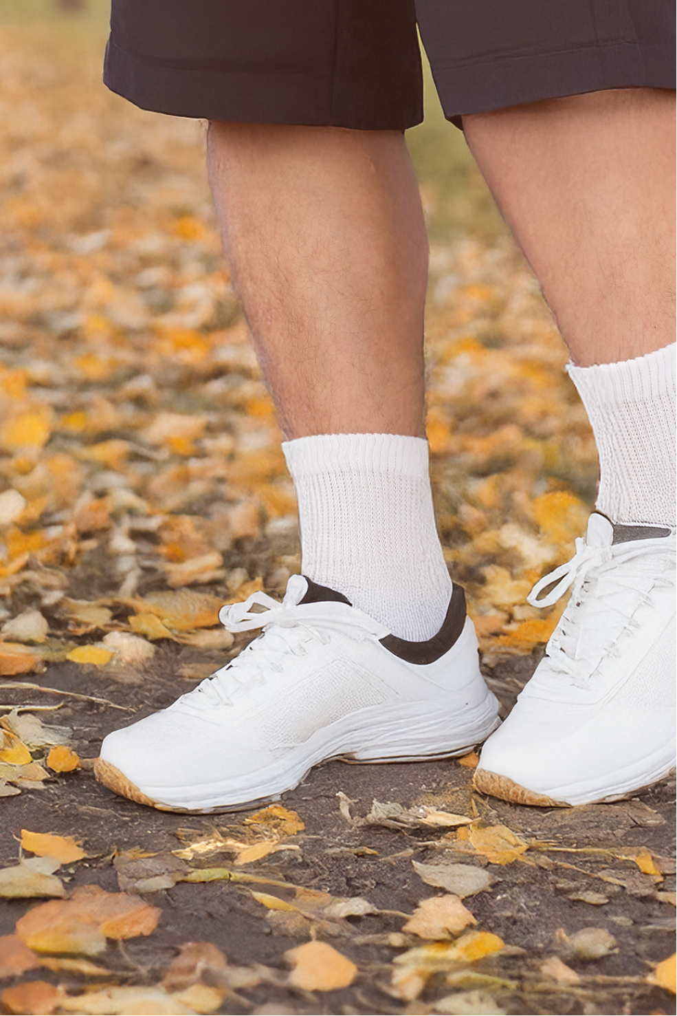 White sneakers with brown accents worn on a person's feet, standing on a ground covered with autumn leaves.
