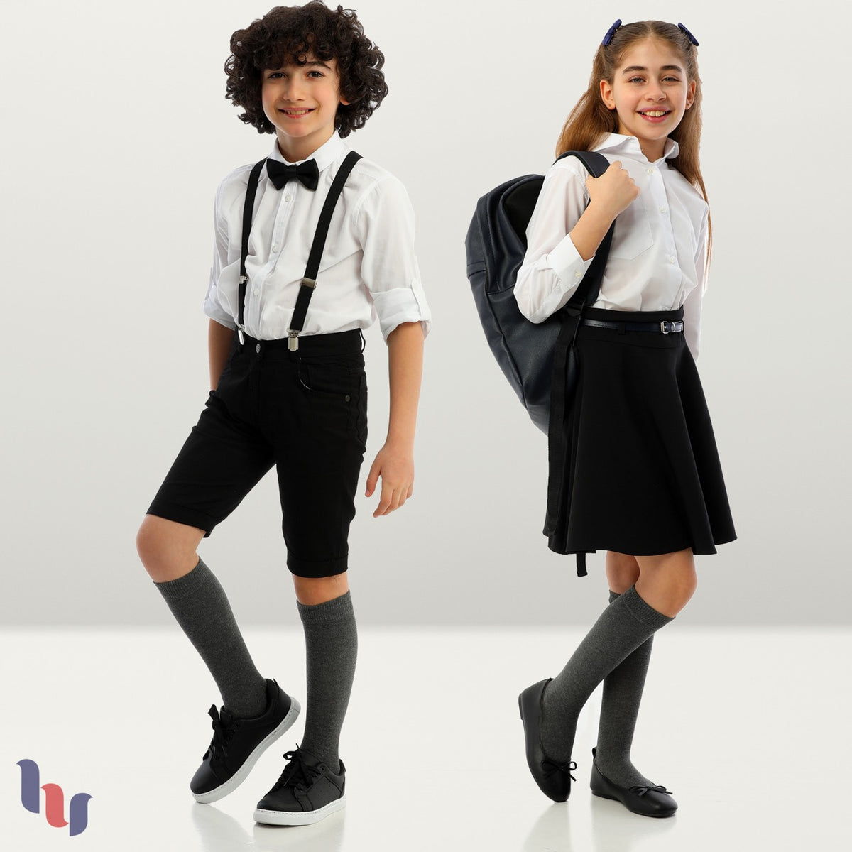 Two young students dressed in school uniforms and carrying backpacks, wearing Kids' Cotton Knee-High socks.