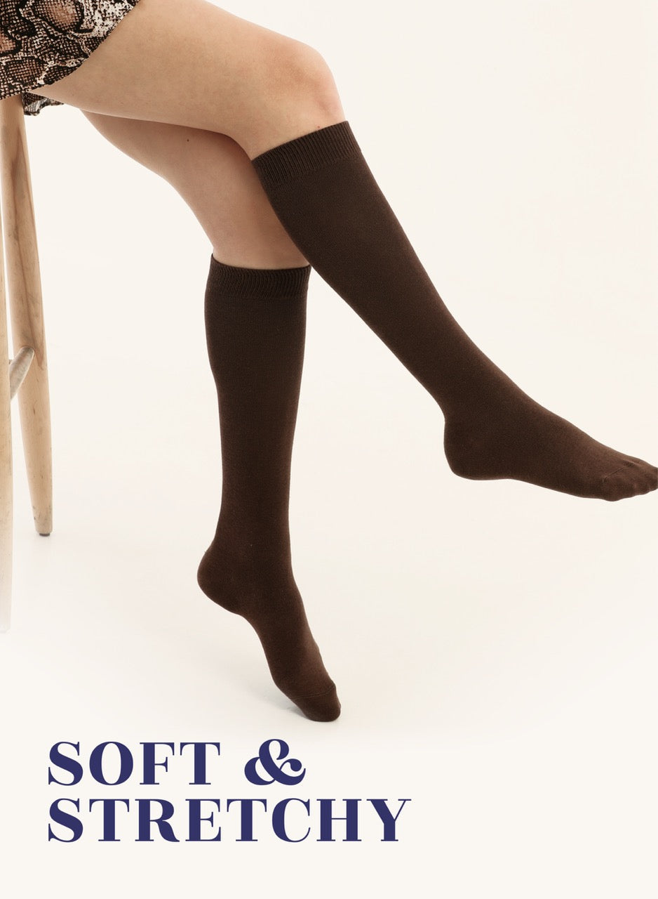 Brown knee-high socks worn by a person sitting on a chair with 'Soft & Stretchy' text.