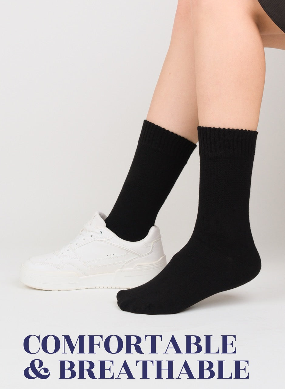 Person wearing black socks with white sneakers on a light gray background