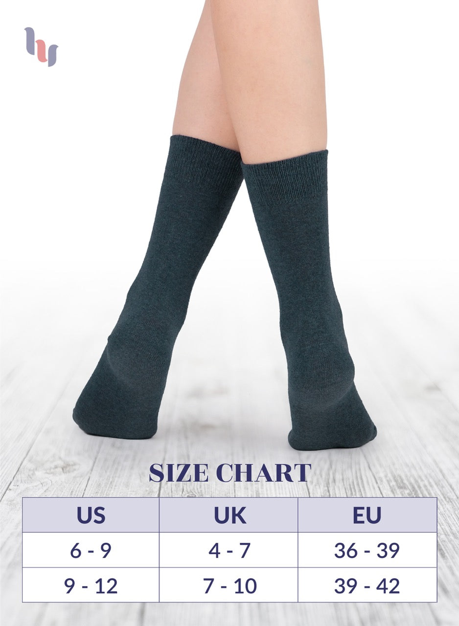 Black knee-high socks on a person's legs with a size chart below on a light wooden floor.