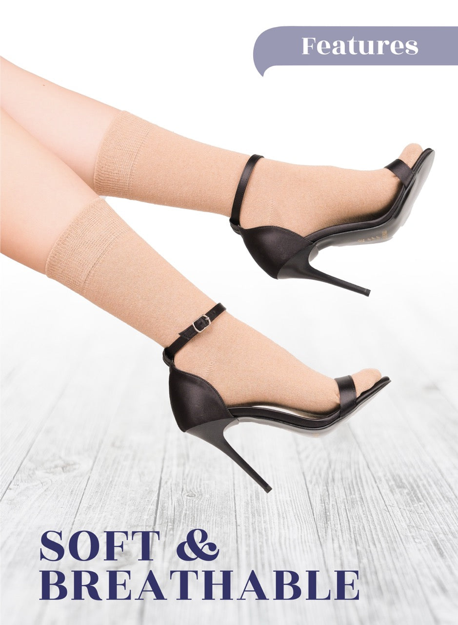 Black high-heeled shoes worn with light beige stockings on a light wooden floor.