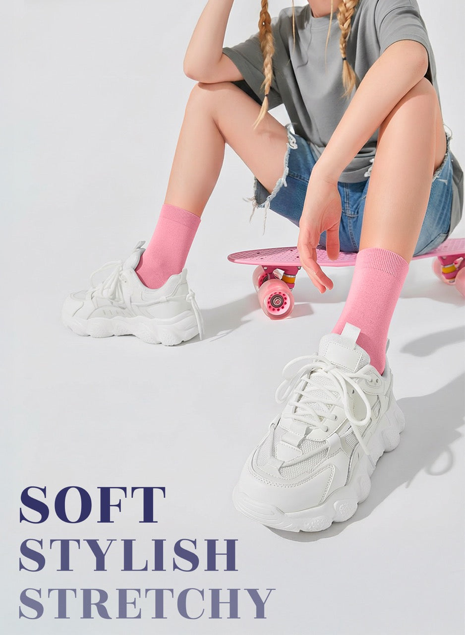 Person sitting on a skateboard wearing white sneakers, pink socks, and denim shorts with text 'SOFT STYLISH STRETCHY'.