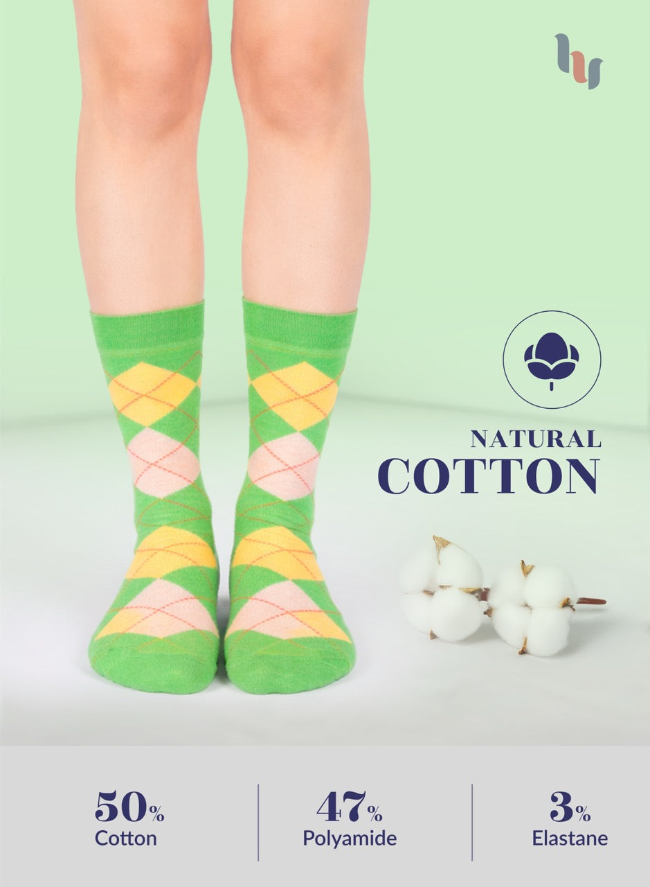 Green argyle socks with pink and yellow diamonds worn by a person on a light green background, featuring natural cotton label and material composition text.