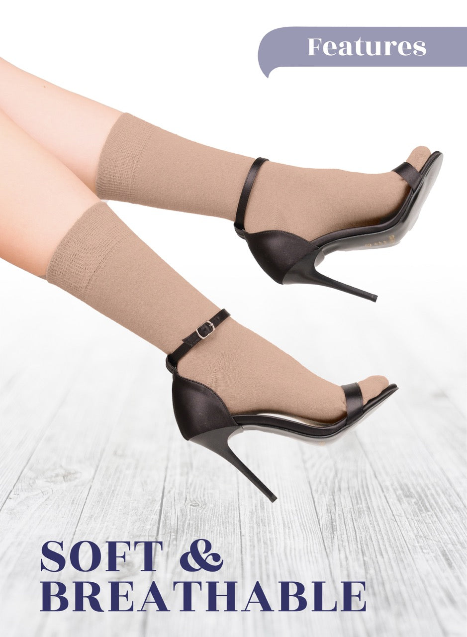 Black high-heeled shoes worn with beige socks on a light wooden floor.