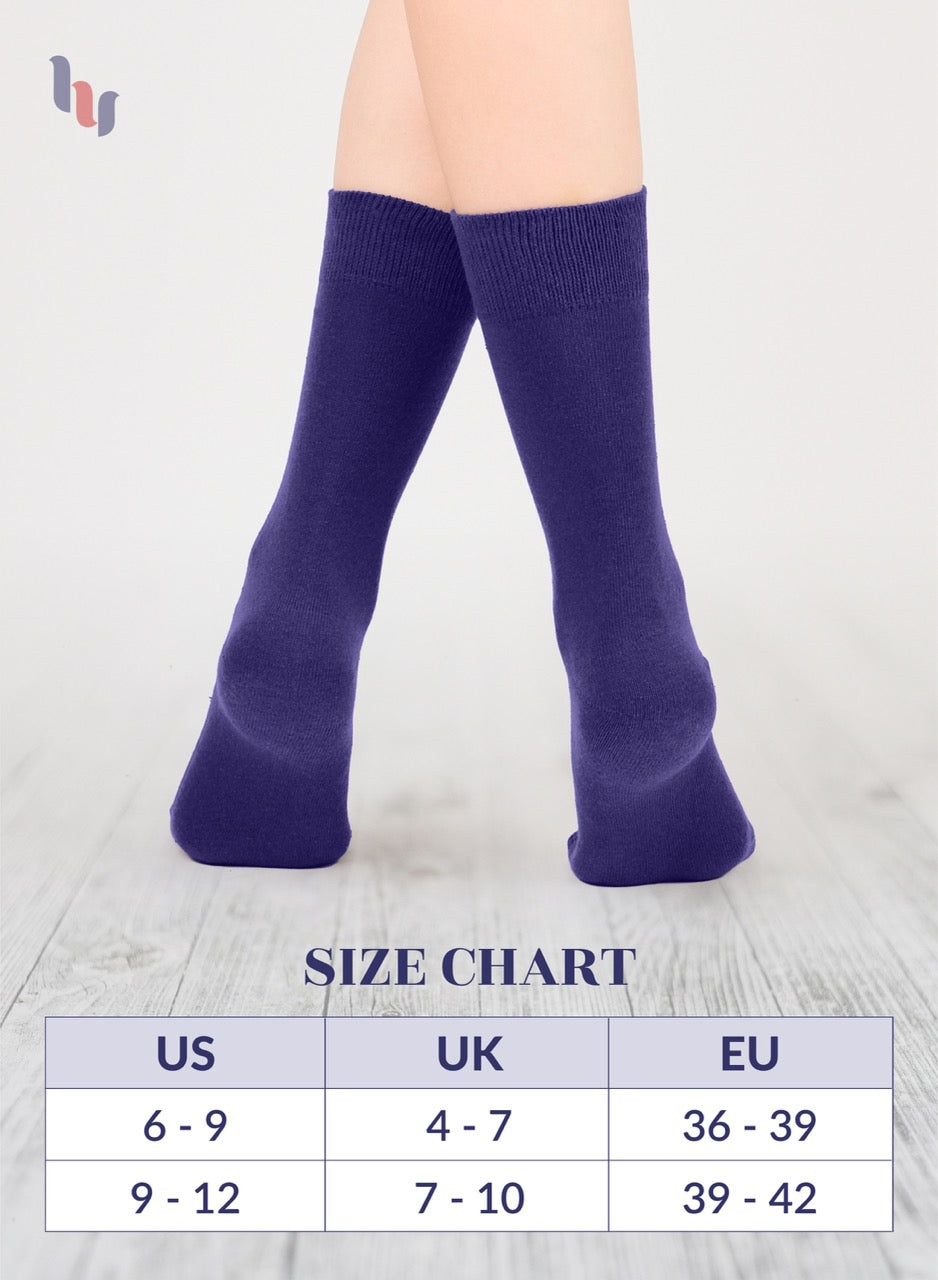 Purple crew socks worn by a person on a light wooden floor with a size chart below.