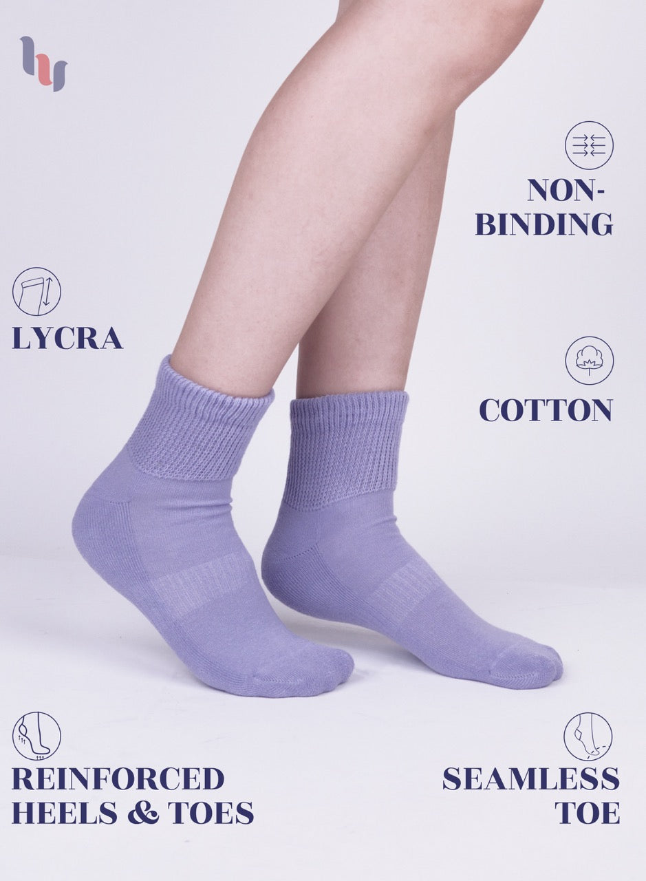 Aster purple socks worn by a person on a light gray background with text highlighting features like 'lycra', 'non-binding', 'cotton', 'reinforced heels & toes', and 'seamless toe'.