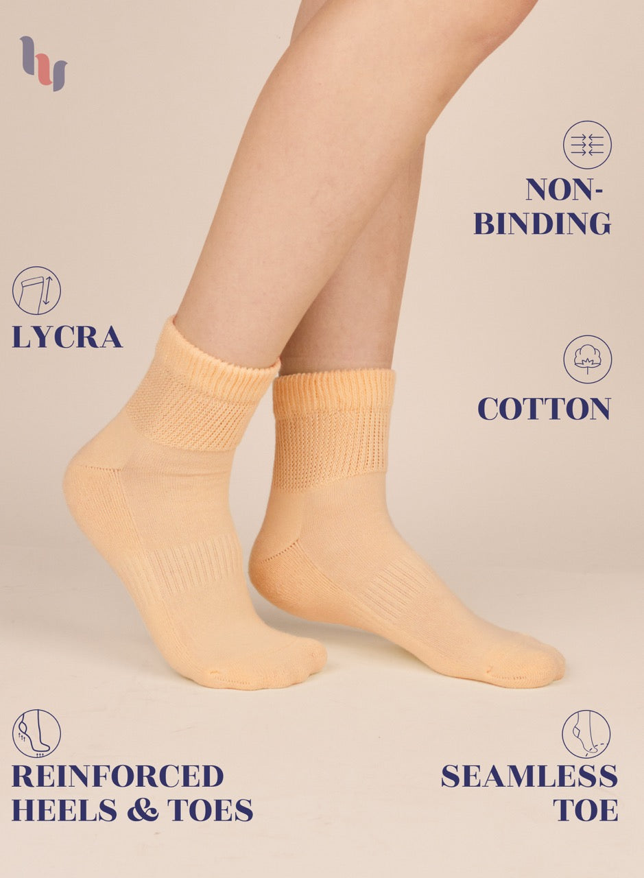 Pastel peach socks worn by a person on a beige background with text highlighting features like 'lycra', 'non-binding', 'cotton', 'reinforced heels & toes', and 'seamless toe'.