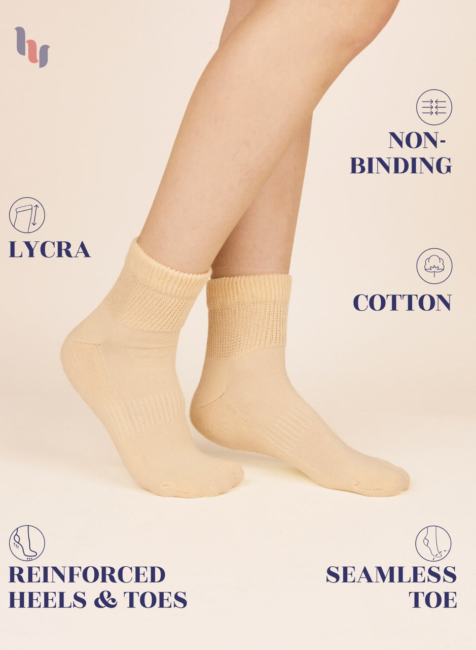 Pastel yellow socks worn by a person on a beige background with text highlighting features like 'lycra', 'non-binding', 'cotton', 'reinforced heels & toes', and 'seamless toe'.