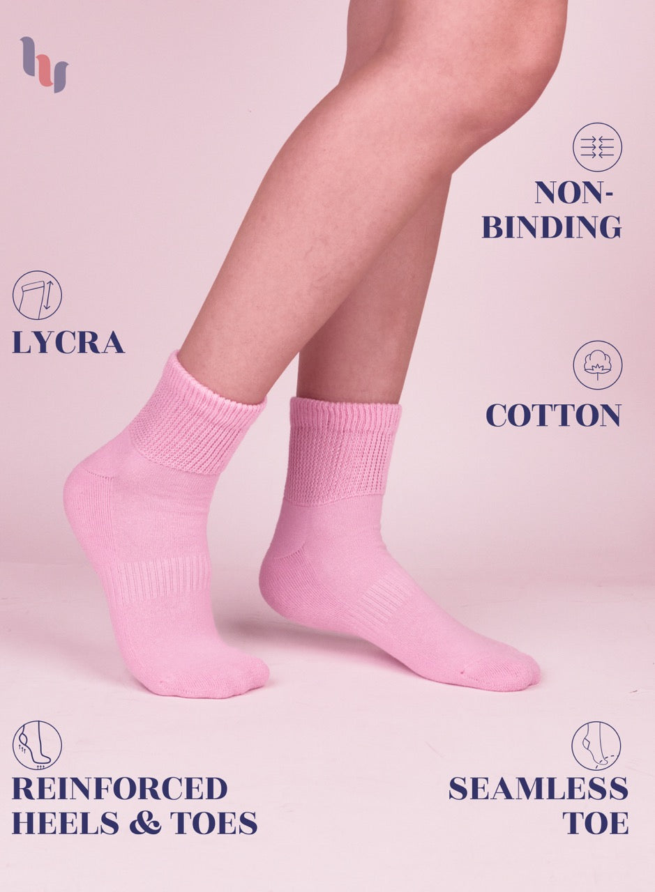 Pink socks worn by a person on a pink background with text highlighting features like LYCRA, non-binding, cotton, reinforced heels & toes, and seamless toe.