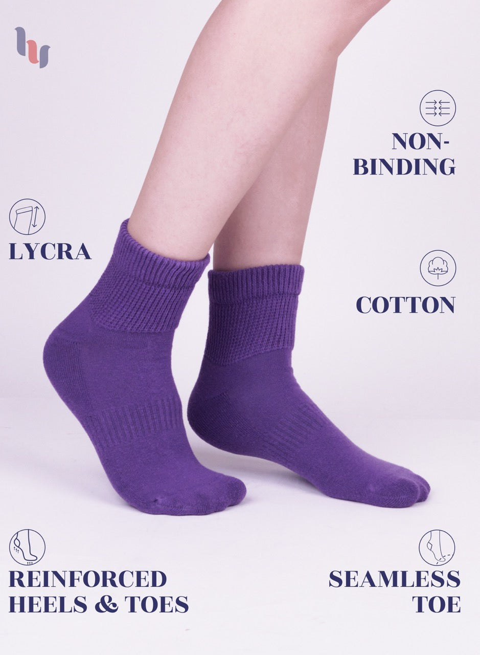 Purple socks worn by a person on a light purple background with text highlighting features like 'lycra', 'non-binding', 'cotton', 'reinforced heels & toes', and 'seamless toe'.