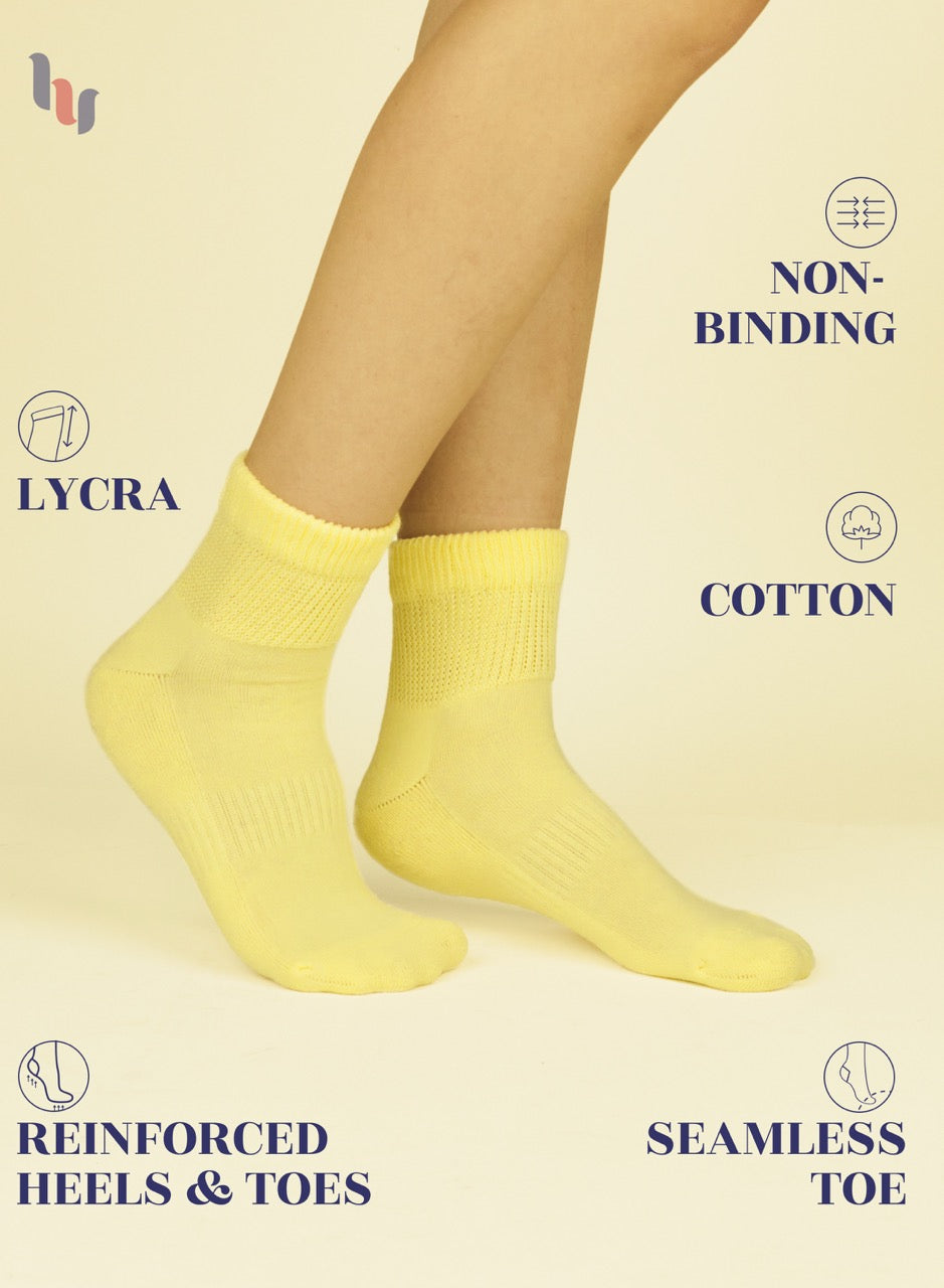 Yellow socks being worn on a beige background with text highlighting features like 'lycra', 'non-binding', 'cotton', 'reinforced heels & toes', and 'seamless toe'.