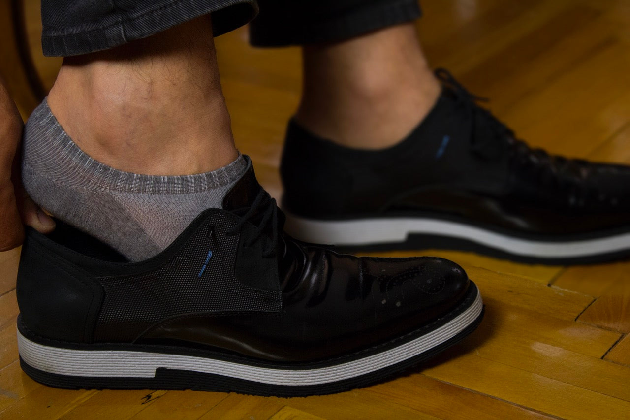 The image depicts an individual donning black shoes and Cotton No-Show Plain Socks, which are barely visible due to their low-cut design.