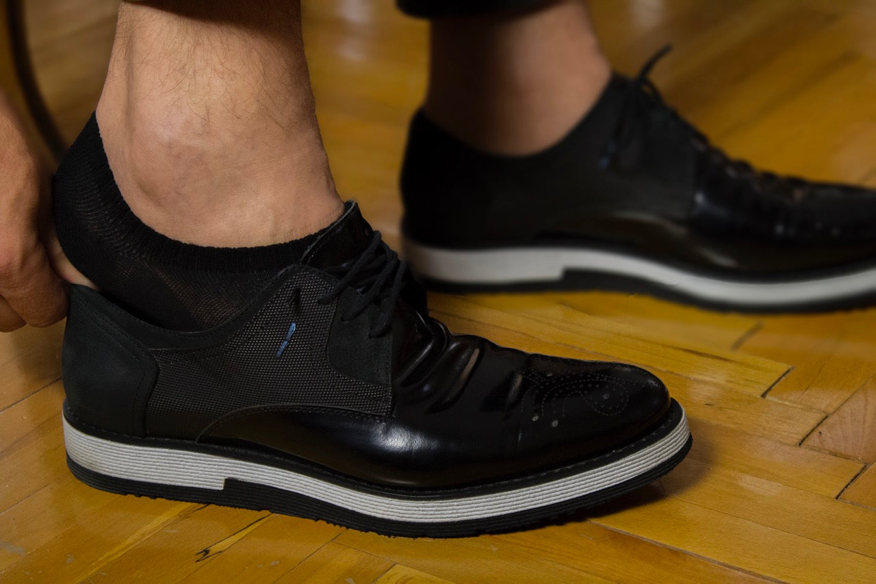 A gentleman is fastening his shoelaces on a wooden surface while wearing Cotton No-Show Plain Socks.