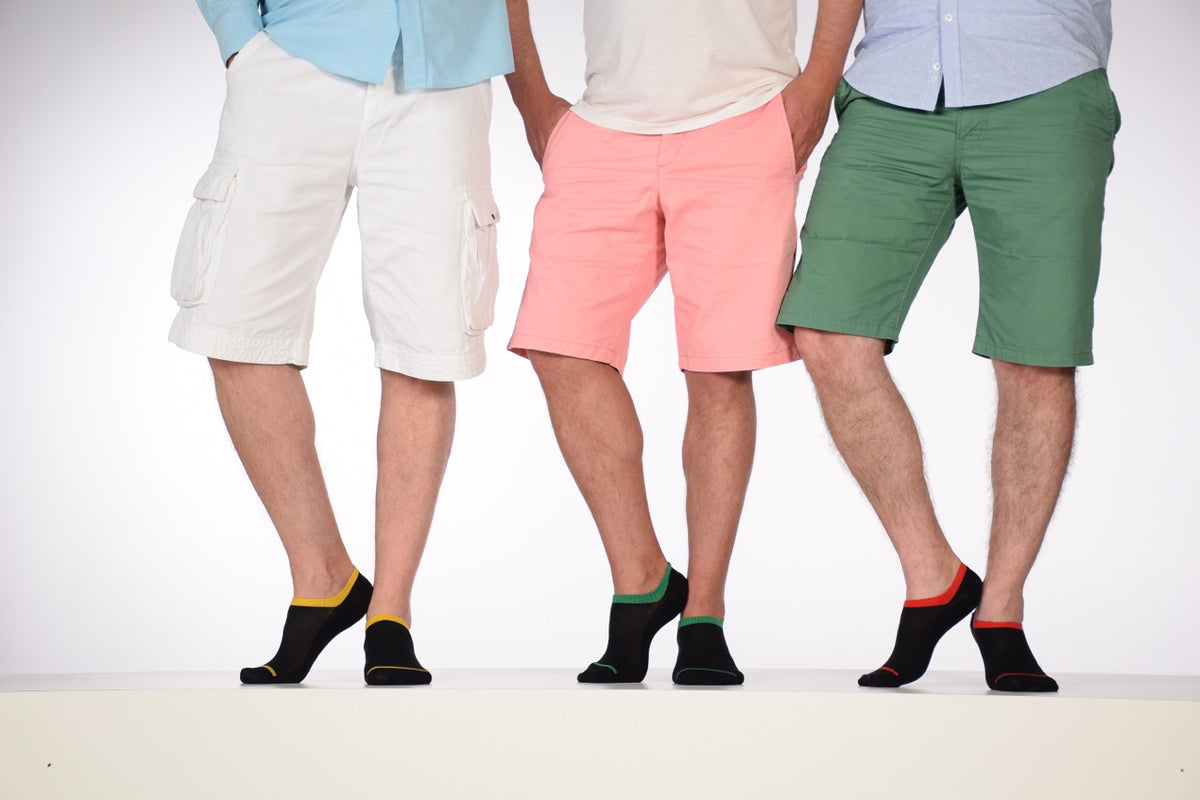 Three men sporting Cotton No-Show Socks for Men stand on a white surface, donning shorts and socks.
