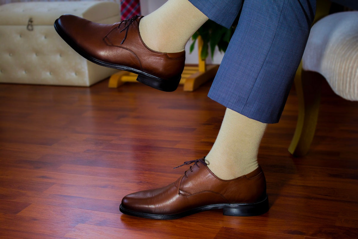 A man in formal attire sits on a wooden floor, showcasing his Cotton Crew Socks.